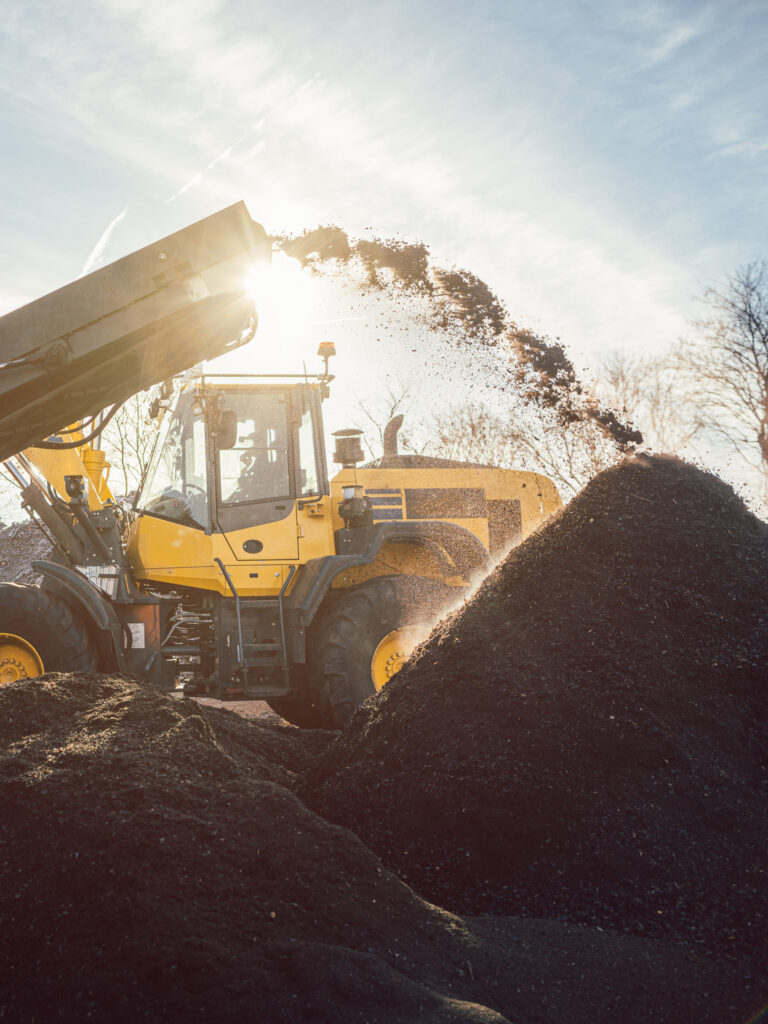 Heavy machinery moving earth and biomass in compost works